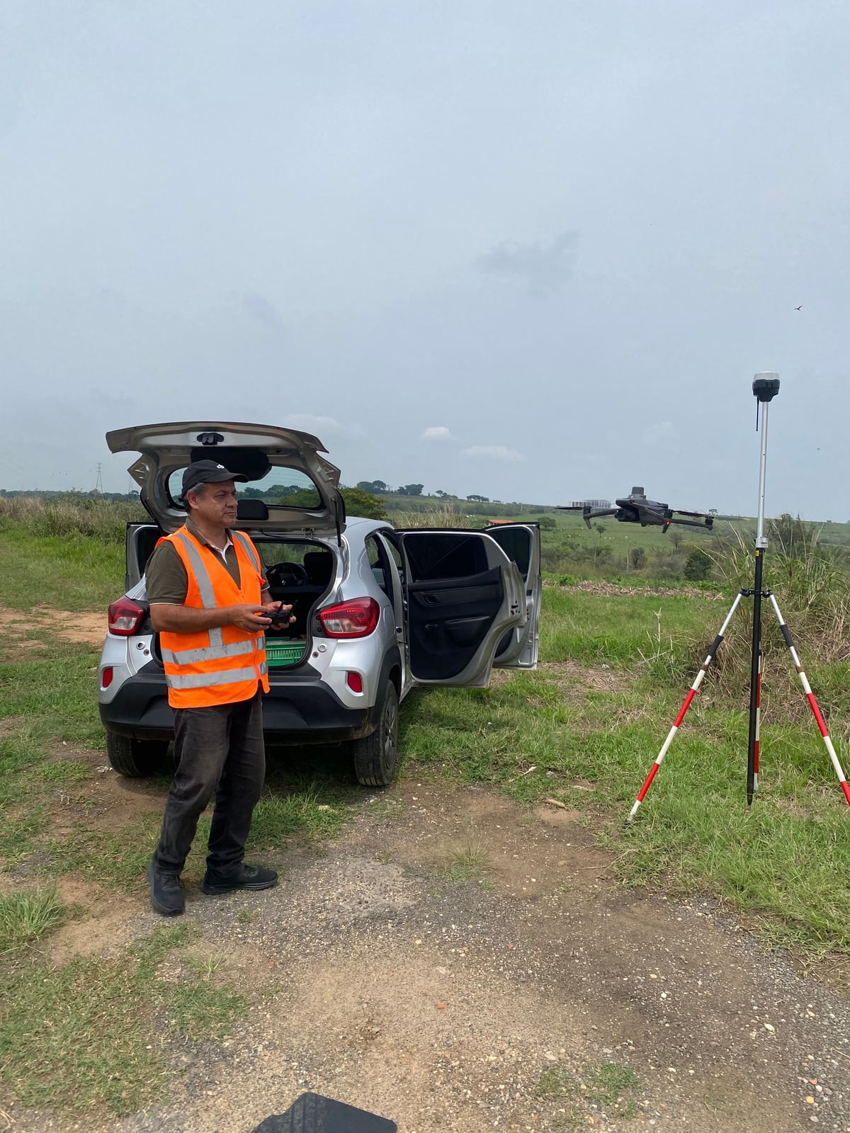 Piloto operando a aeronave remotamente pilotada, com o receptor GNSS montado no tripé ao lado